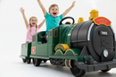 Two happy children riding a green electric Classic Railroad ride-on train toy with their arms raised in excitement. The train is trackless so it can ride anywhere.