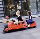 Two children playing with a toy train on a street.